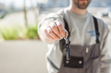 Hand holding a car key outdoors, blurred background, shallow focus.